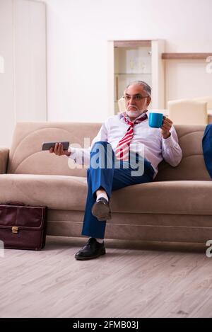 Leitender männlicher Chef-Angestellter, der zu Hause Fernsehen schaut Stockfoto