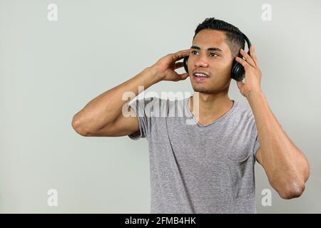 Der 28-jährige Brasilianer hält mit beiden Händen kabellose Kopfhörer, hört Musik und blickt auf den Horizont. Stockfoto