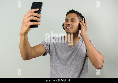Lächelnder 28-jähriger Brasilianer, der ein Foto von sich selbst macht, mit einer Hand auf dem kabellosen Kopfhörer. Stockfoto