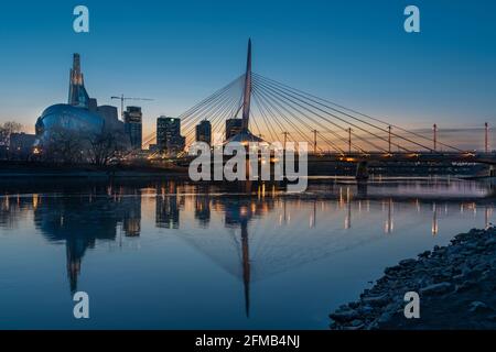 Die Stadt Sklyline beleuchtet bei Sonnenuntergang spiegelt sich im Red River, Windnypeg, Manitoba, Kanada. Stockfoto