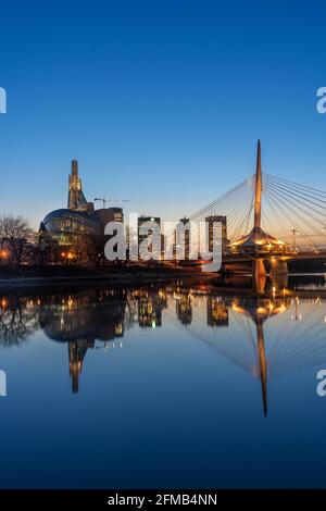 Die Stadt Sklyline beleuchtet bei Sonnenuntergang spiegelt sich im Red River, Windnypeg, Manitoba, Kanada. Stockfoto