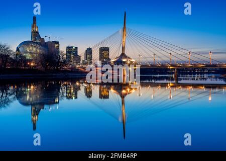 Die Stadt Sklyline beleuchtet bei Sonnenuntergang spiegelt sich im Red River, Windnypeg, Manitoba, Kanada. Stockfoto