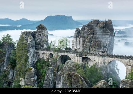 Deutschland, Sachsen, Nationalpark Sächsische Schweiz, Elbsandsteingebirge, Blick auf die Bastei-Brücke am Morgen, Nebel im Elbtal, hinter dem Lilienstein Stockfoto
