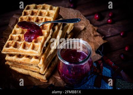 Waffeln auf Kühlregalen gestapelt mit einem Klecks hausgemachter Preiselbeermarmelade, Einmachglas, Löffel, launische Stimmung Stockfoto