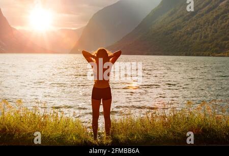 Frau am Ufer eines Bergsees bei Sonnenaufgang Stockfoto