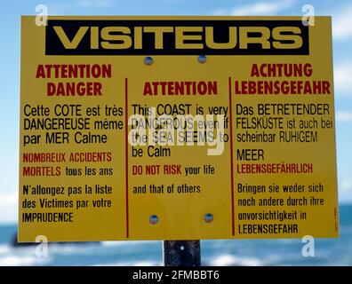 Warnschild für Touristen an einer felsigen Küste in drei Sprachen unberechenbarer Gefahren Stockfoto