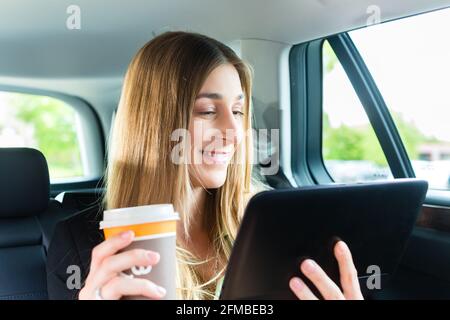 Junge Geschäftsfrau unterwegs im Taxi, sie halten Tasse Kaffee und einem Tablet-computer Stockfoto