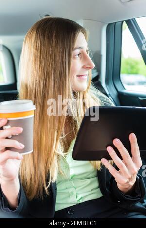 Junge Geschäftsfrau unterwegs im Taxi, sie halten Tasse Kaffee und einem Tablet-computer Stockfoto