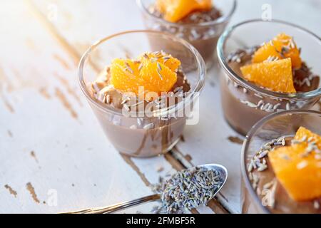 Ayurvedische Küche - Schokoladenmousse mit seidenem Tofu, dekoriert mit Orangenfilets und Lavendelblüten, gefüllte kleine Glasschüsseln stehen auf einem weißen Holztisch Stockfoto