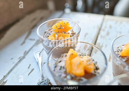 Ayurvedische Küche - Schokoladenmousse mit seidenem Tofu, dekoriert mit Orangenfilets und Lavendelblüten, gefüllte kleine Glasschüsseln stehen auf einem weißen Holztisch Stockfoto