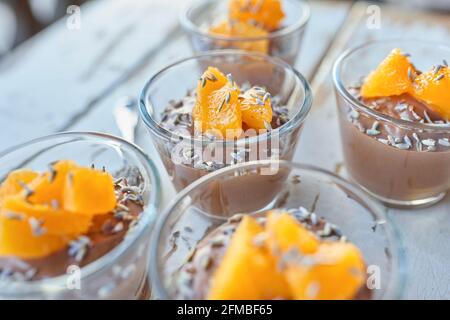 Ayurvedische Küche - Schokoladenmousse mit seidenem Tofu, dekoriert mit Orangenfilets und Lavendelblüten, gefüllte kleine Glasschüsseln stehen auf einem weißen Holztisch Stockfoto