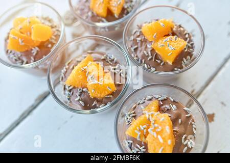 Ayurvedische Küche - Schokoladenmousse mit seidenem Tofu, dekoriert mit Orangenfilets und Lavendelblüten, gefüllte kleine Glasschüsseln stehen auf einem weißen Holztisch Stockfoto