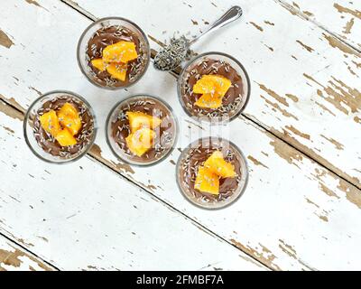 Ayurvedische Küche - Schokoladenmousse mit seidenem Tofu, dekoriert mit Orangenfilets und Lavendelblüten, gefüllte kleine Glasschüsseln stehen auf einem weißen Holztisch Stockfoto