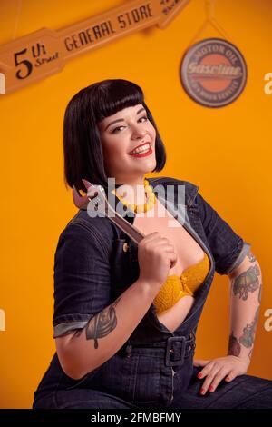 Tätowierte kurvige Modell mit schwarzen Haaren in Pin-up-Stil als Ein Mechaniker Stockfoto