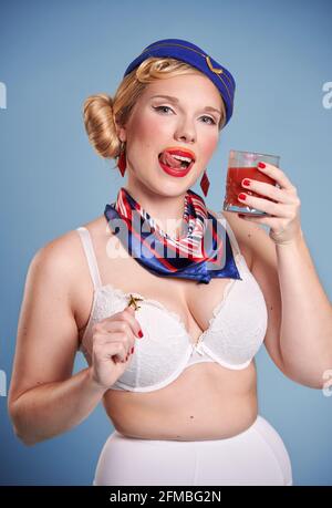 Blonde junge Frau als Stewardess im Pin-up-Look mit Tomatensaft Stockfoto