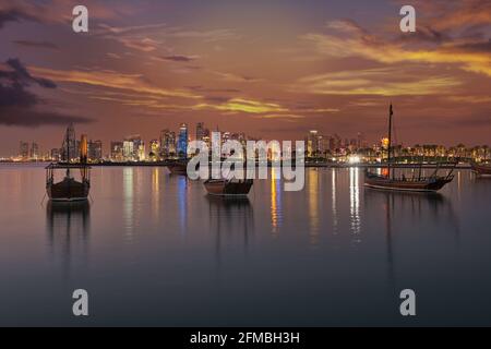 Doha Katar Skyline in der Abenddämmerung zeigt Wolkenkratzer Lichter reflektiert in Der arabische Golf und Daus im Vordergrund mit Wolken in Der Himmel im Hintergrund Stockfoto