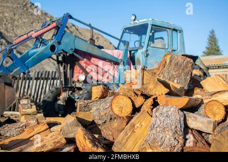 Ein Haufen gesägtes Holz, Keile, liegt auf dem Hof auf der Straße im Dorf vor dem Hintergrund eines alten Traktors Stockfoto