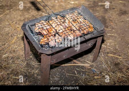 Stücke von frischem Fleisch werden in einem Grill, der auf einem heißen Grill mit Kohlen in der Nacht unter dem künstlichen Licht der Lampen liegt platziert Stockfoto