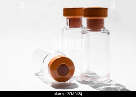 Drei aufrechte und eine horizontale Vials für medizinische Impfstoffe mit orangefarbenen Kappen. Von der Sonne hinterleuchtet, weißer Hintergrund Stockfoto