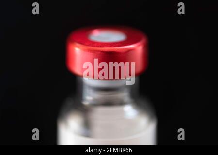 Oberteil einer Impfstoffflasche mit rotem Verschluss auf schwarzem Hintergrund. Flüssigkeit zur Injektion. Konzentrieren Sie sich auf den roten Fläschchendeckel, geringe Schärfentiefe Stockfoto