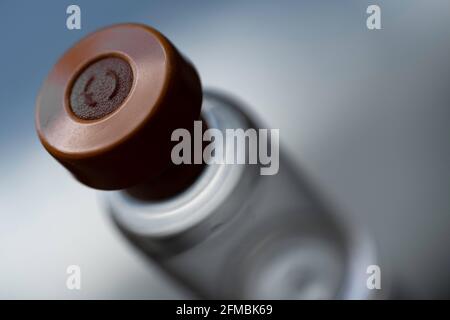 Geheimnisvolles Bild eines Impfstofffläschchens mit orangefarbener Kappe auf einem dunklen, unscharfen Hintergrund. Flüssigkeit zur Injektion. Konzentrieren Sie sich auf die Gummimitte der Kappe Stockfoto