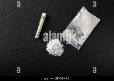 Kokain in einer Plastikverpackung auf schwarzem Hintergrund, Nahaufnahme. Eine zusammengerollte Dollar-Rechnung für Drogenkonsum. Verbotene Drogen. Stockfoto