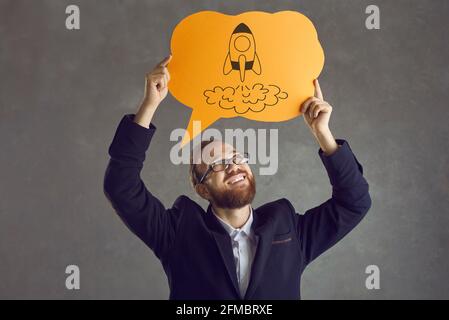 Glücklicher Geschäftsmann in Anzug und Brille halten Sprechballon mit Bild der Weltraumrakete Stockfoto