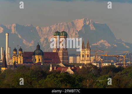 München, Deutschland. Mai 2021. In den frühen Morgenstunden vor der Kulisse der rund 90 Kilometer entfernten Alpen sind Schornsteine des Heizkraftwerks Süd (l-r), der Theatinerkirche, der Frauenkirche und der Sankt Ludwig-Kirche der bayerischen Hauptstadt zu sehen. (Das Bild wurde mit einem 800 Millimeter Teleobjektiv aufgenommen) Quelle: Peter Kneffel/dpa/Alamy Live News Stockfoto