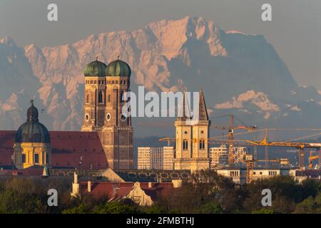 München, Deutschland. Mai 2021. Die Theatinerkirche (l-r), die Frauenkirche und die Sankt Ludwig-Kirche der bayerischen Hauptstadt sind in den frühen Morgenstunden vor der Kulisse der Alpen mit der Zugspitze in etwa 90 Kilometern Entfernung zu sehen. (Das Bild wurde mit einem 1120 Millimeter Teleobjektiv aufgenommen) Quelle: Peter Kneffel/dpa/Alamy Live News Stockfoto