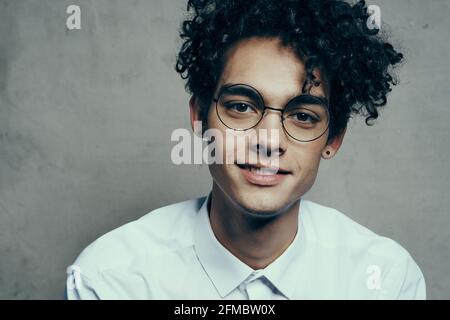 Lockiger Mann mit Brille und weißem Hemd Ein Stoff Hintergrund Lächeln Modell Nahaufnahme Porträt Stockfoto