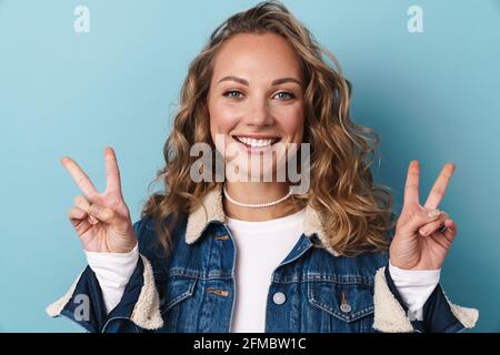 Blonde glückliche Frau lächelt und gestikuliert Friedensschild isoliert Blaue Wand Stockfoto
