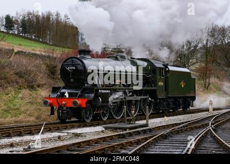 Historische Dampflok (grün glänzende Lok), stationär auf der Strecke, Rauchwolken auf der malerischen ländlichen Heritage Railway - KWVR, Yorkshire, England, Großbritannien. Stockfoto