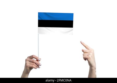 Eine schöne weibliche Hand hält eine estnische Flagge, auf der sie den Finger ihrer anderen Hand zeigt, isoliert auf weißem Hintergrund. Stockfoto