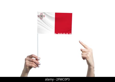 Eine schöne weibliche Hand hält eine Malta-Flagge, auf der sie den Finger ihrer anderen Hand zeigt, isoliert auf weißem Hintergrund. Stockfoto