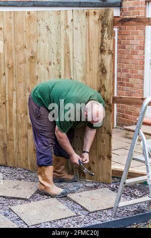 Ein Mann, der Nägel in ein Brett und einen Zaun eingeschlagen hat Er hat gerade in einem Garten in Stockton On errichtet T-Shirts, England, Großbritannien Stockfoto