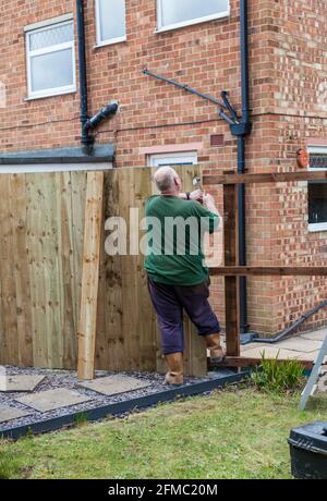 Ein Mann, der Nägel in ein Brett und einen Zaun eingeschlagen hat Er hat gerade in einem Garten in Stockton On errichtet T-Shirts, England, Großbritannien Stockfoto