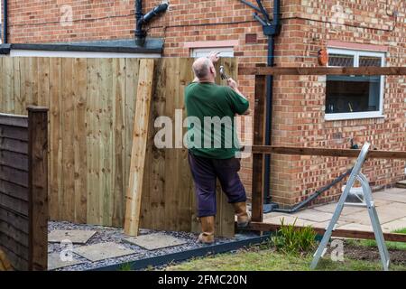 Ein Mann, der Nägel in ein Brett und einen Zaun eingeschlagen hat Er hat gerade in einem Garten in Stockton On errichtet T-Shirts, England, Großbritannien Stockfoto