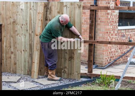 Ein Mann, der Nägel in ein Brett und einen Zaun eingeschlagen hat Er hat gerade in einem Garten in Stockton On errichtet T-Shirts, England, Großbritannien Stockfoto