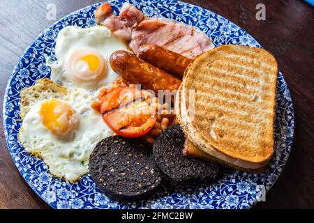 Teller mit schottischem Frühstück mit zwei Spiegeleiern, Speck, zwei Würstchen, zwei schwarzen Puddings, gebackenen Bohnen, Kartoffelbrot, Tomaten und zwei Scheiben Toast. Stockfoto