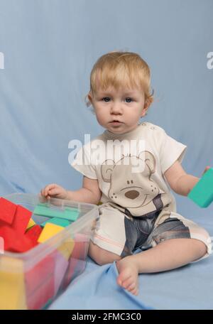 Ein kleines blondes Mädchen in einem kurzen Jumpsuit mit einem Bär Muster und spielen mit bunten Würfel Konstruktor Stockfoto