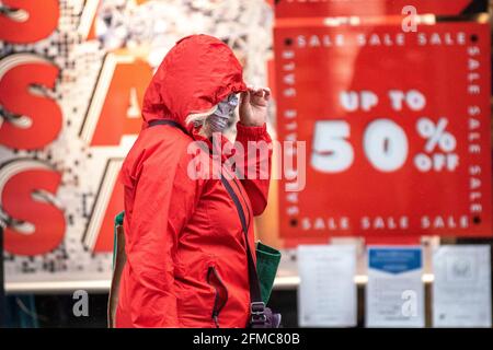 Frau in rotem Anorak, die 50 %-Verkaufsschild in Preston, Lancashire, Großbritannien, passiert. Mai 2021. UK Wetter; nasser und windiger Tag im Stadtzentrum. Es wird erwartet, dass die Südwinde im Laufe des Tages mildere Temperaturen bringen werden. Credit MediaWorldImages/AlamyLiveNews Stockfoto