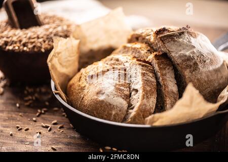 Schöne knusprige Hefebrotscheiben auf dem Backpapier in der legierten rustikalen Pfanne auf dem Holztisch mit Vollkorngetreide im Hintergrund serviert. Stockfoto