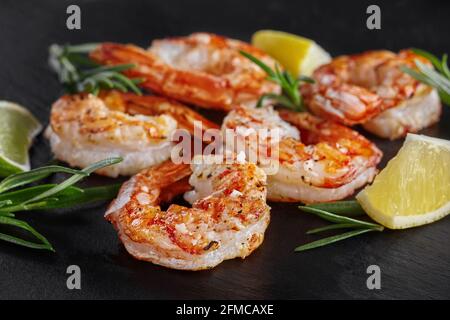 Gebratene Scampi-Schwänze mit Limette, Zitrone und Rosmarin auf schwarzem Hintergrund Stockfoto