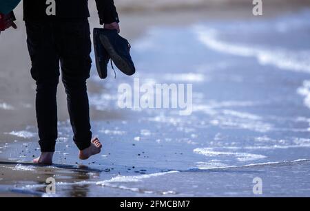 Pommern, Deutschland. Mai 2021. 08. Mai 2021, Mecklenburg-Vorpommern, Warnemünde: Am Strand von Warnemünde spaziert ein Mann barfuß durch die kühle Ostsee. Das teilweise sonnige Wetter mit Temperaturen um die 15 Grad lockte Tagesausflügler an die Ostseeküste Mecklenburg-Vorpommerns. Quelle: dpa picture Alliance/Alamy Live News Stockfoto