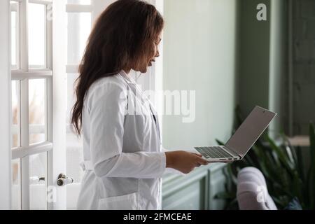 Gutaussehende, zufriedene afroamerikanische Ärztin, die an einem Laptop arbeitet. Telemedizin Stockfoto