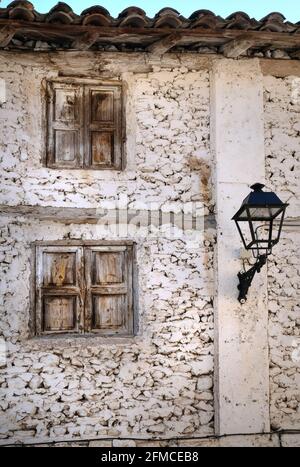 Ein altes und heruntergekommenes Haus mit einer Straßenlampe an der weißgetünchten Steinmauer in Libros, in der Nähe von Teruel, Aragon, Spanien. Verwitterte Holzläden sind geschlossen Stockfoto