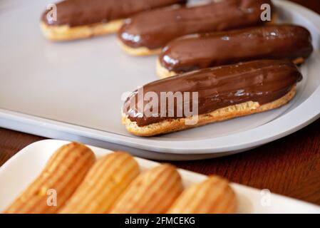 Französische Dessert-Eclare oder Profiterolen mit dunkler Schokoladenglasur. Kuchen mit Rahm und Belag. Weicher, selektiver Fokus. Stockfoto