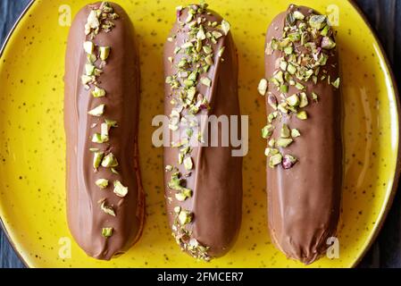 Französische Dessert-Eclare oder Profiteroles mit Milchschokoladenglasur und Pistazien. Kuchen mit Rahm und Belag. Weicher, selektiver Fokus. Stockfoto