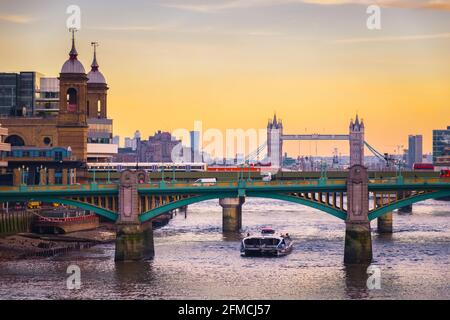 Orangefarbener Sonnenuntergang mit dem Stadtbild Londons, einschließlich Cannon Street Railway Bridge, Southwark Bridge und Tower Bridge Stockfoto