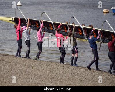 Putney, Greater London, England - 04 2021. Mai: Jugendliche tragen ein Ruderboot zur Vorbereitung auf das Training an die Themse. Stockfoto